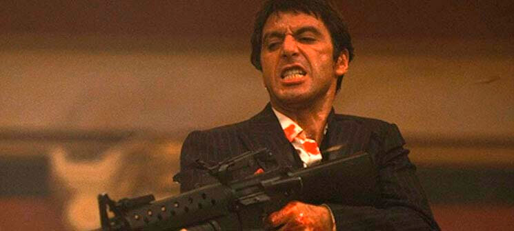 Tony Montana interpretado por Al Pacino segurando uma metralhadora em Scarface. Um dos personagens mais famosos dos anos 80. 