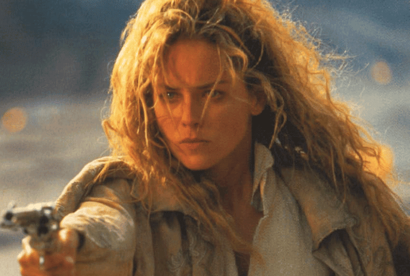 Ellen (Sharon Stone) com trajes de cowgirl segurando um revolver em Rápida e Mortal. 30 personagens femininas que marcaram a história do cinema